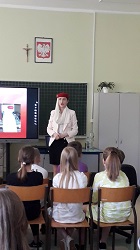 Na zdjęciu znajduje się stewardessa oraz uczniowie klasy IV, którzy siedzą na krzesłach i są odwróceni tyłem