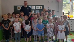 Na zdjęciu znajdują się dzieci z grupy biedronki oraz klasy 0. Za nimi stoi uśmiechnięty policjant