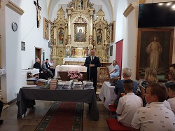 Na zdjęciu na środku ołtarza stoi Burmistrz, który przemawia. Po  jego lewej stronie znajduje się ksiądz oraz uczniowie szkoły. Z przodu na ławkach siedzi Pani Dyrektor , uczniowie szkoły oraz rodzice